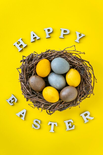 Huevos de Pascua multicolores en nido de pájaros sobre fondo amarillo Letras de Pascua feliz Marco vertical