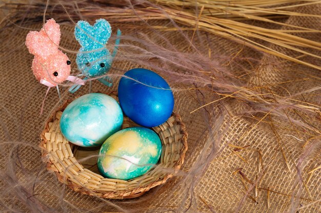 Huevos de Pascua multicolores de tonos azules y dos conejitos de Pascua en un palo sobre un fondo de tela