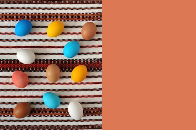 Huevos de Pascua multicolores yacen sobre un mantel bordado Espacio para texto sobre fondo rosa melocotón