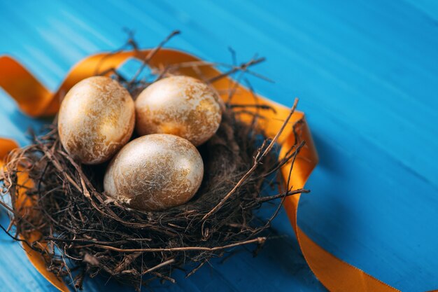 Huevos de Pascua en el nido en la superficie de madera azul con cinta dorada