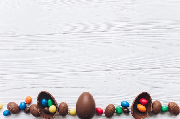 Huevos de Pascua y orejas de conejo de chocolate en el fondo de madera blanco.