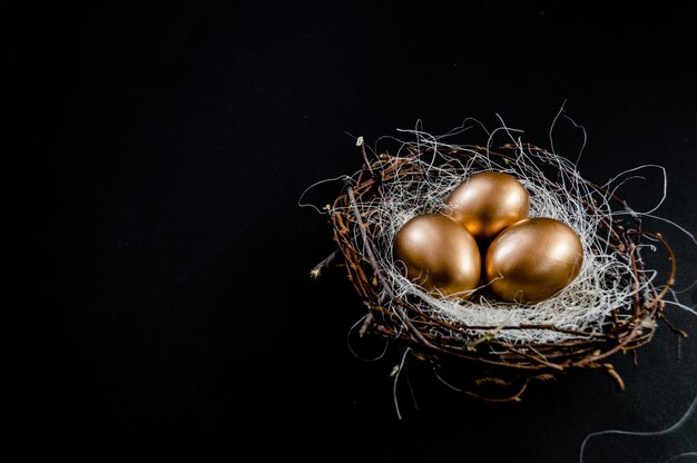 Los huevos de Pascua de oro en pájaros jerarquizan en fondo negro. Opinión superior del copyspace del fondo del extracto del concepto del día de fiesta de Pascua varios objetos.