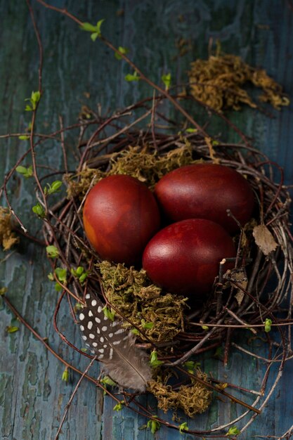 Huevos de Pascua en un pequeño nido hecho de ramas y musgo sobre un fondo de madera