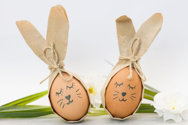 Huevos de Pascua pintados como conejitos con flores en una pared blanca.