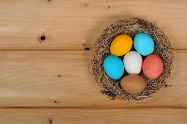 Huevos de pascua pintados en diferentes colores en un nido sobre un fondo de tablas de madera