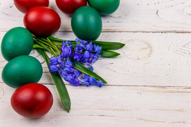 Huevos de Pascua pintados y flores de scilla azul sobre fondo blanco de madera Composición de Pascua Vista superior espacio de copia