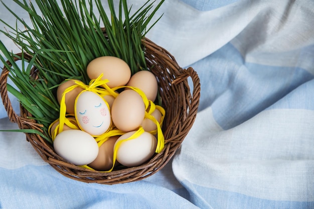 Huevos de Pascua pintados, un huevo con una cara linda, los huevos yacen en una canasta de madera junto con hierba verde. Postal de Pascua.