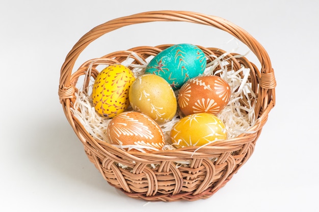 Huevos de Pascua pintados a mano en canasta marrón sobre blanco