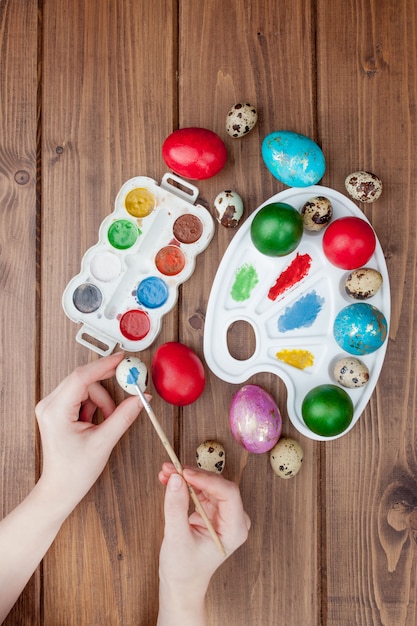 Huevos de Pascua pintados a mano, pinturas y pinceles sobre fondo de madera. Preparación para las vacaciones. Las manos de las niñas dibujan un patrón