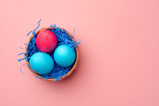 Huevos de Pascua pintados en nido decorativo sobre fondo rosa