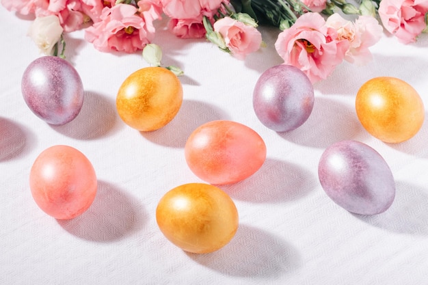 Huevos de Pascua pintados de rosa y morado dorado en colores pastel y ramo de flores sobre un mantel de algodón blanco