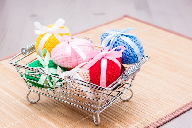 Huevos de Pascua de punto atados con cintas de colores en una canasta de metal sobre una servilleta sobre la mesa