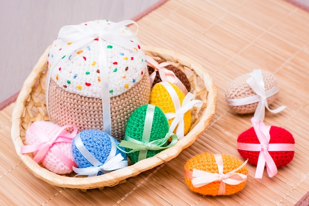 Huevos de Pascua de punto y pastel de Pascua en una cesta de mimbre sobre una mesa de madera