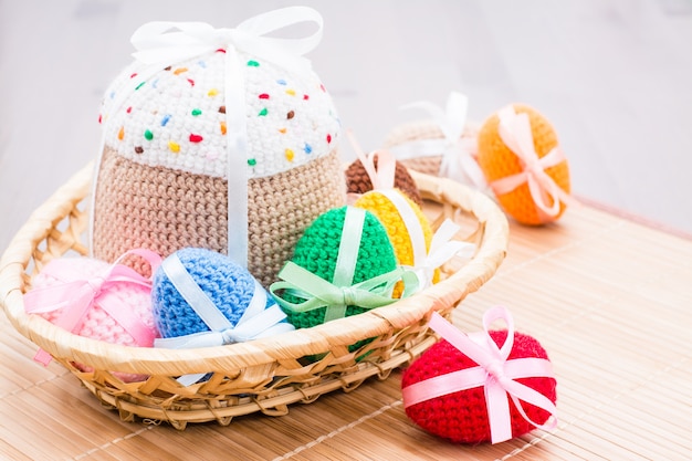 Huevos de Pascua de punto y pastel de Pascua en una cesta de mimbre sobre una mesa de madera