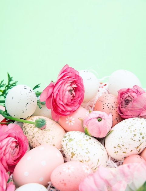 Huevos de Pascua y ramo de flores de ranúnculos rosados en el espacio de copia de fondo verde pastel