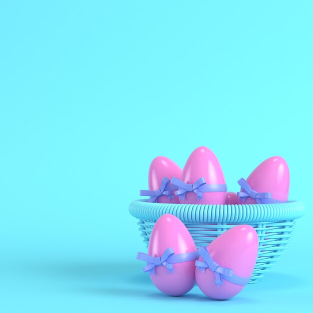 Huevos de pascua rosa con lazo en una canasta de mimbre sobre fondo azul brillante en colores pastel. Concepto de minimalismo