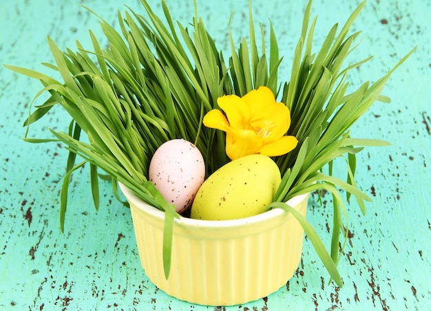 Huevos de Pascua en un tazón con hierba en la mesa de madera verde de cerca