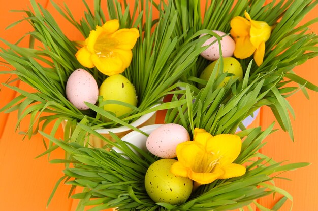 Huevos de Pascua en tazones con hierba en la mesa de madera naranja de cerca