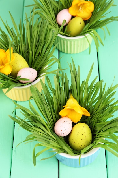 Huevos de Pascua en tazones con hierba en la mesa de madera verde de cerca