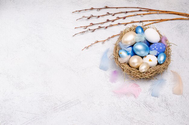 Huevos de Pascua en tonos azules en un nido de paja con ramas de sauce.