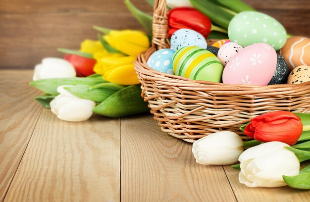 Huevos de pascua y tulipanes en una canasta sobre una mesa de madera