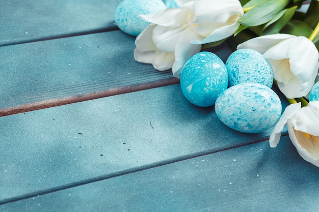 Huevos de Pascua con tulipanes sobre fondo de madera azul