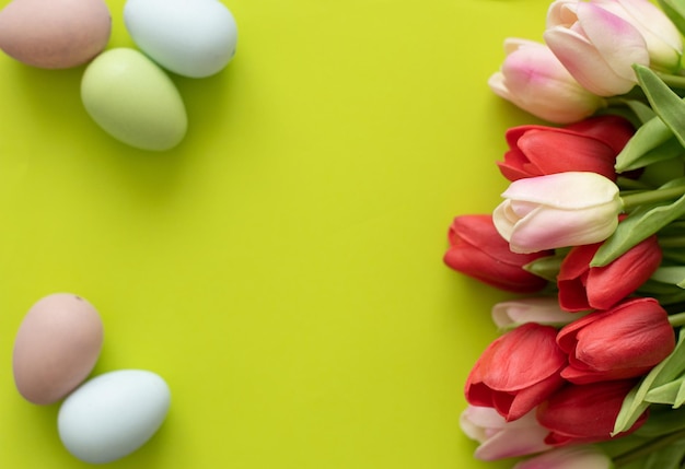 Huevos de Pascua y tulipanes sobre fondo verde claro.