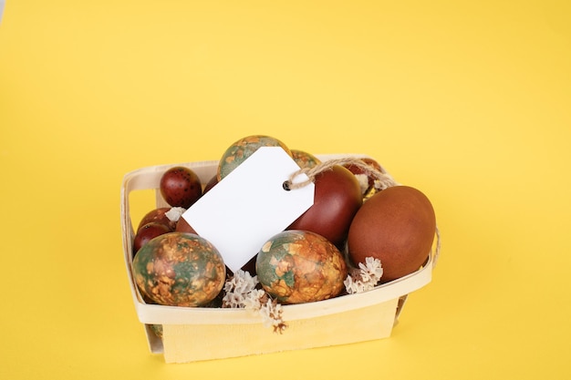 Huevos de Pascua con variados patrones naturales en una pequeña canasta de madera con una etiqueta en blanco