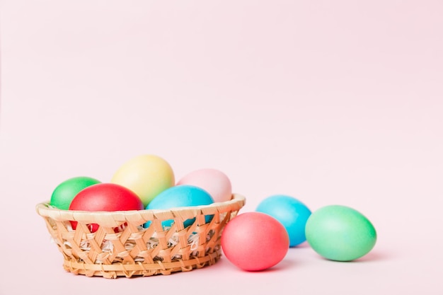 Huevos de Pascua de varios colores en la canasta tejida sobre fondo de color Concepto de vacaciones de huevos de Pascua de color pastel con espacio de copia