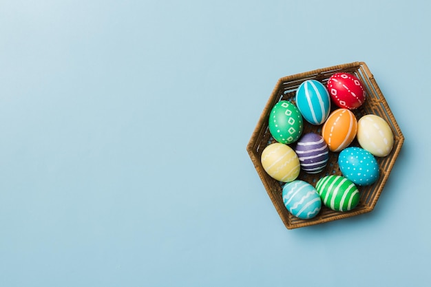 Huevos de Pascua de varios colores en la canasta tejida sobre fondo de color Concepto de vacaciones de huevos de Pascua de color pastel con espacio de copia