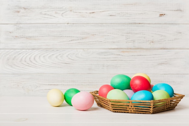 Huevos de Pascua de varios colores en la canasta tejida sobre fondo de color Concepto de vacaciones de huevos de Pascua de color pastel con espacio de copia