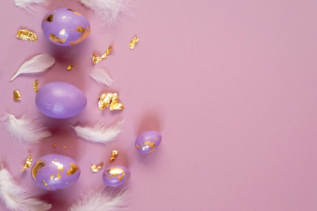 Huevos de pascua violeta o muy peri con lámina dorada y plumas blancas sobre fondo violeta