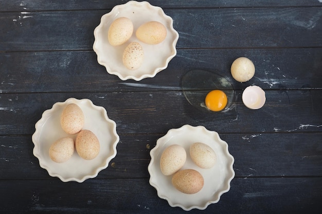 Huevos de pavo en tres platos blancos y un huevo roto en una superficie de madera teñida en bruto horizontal