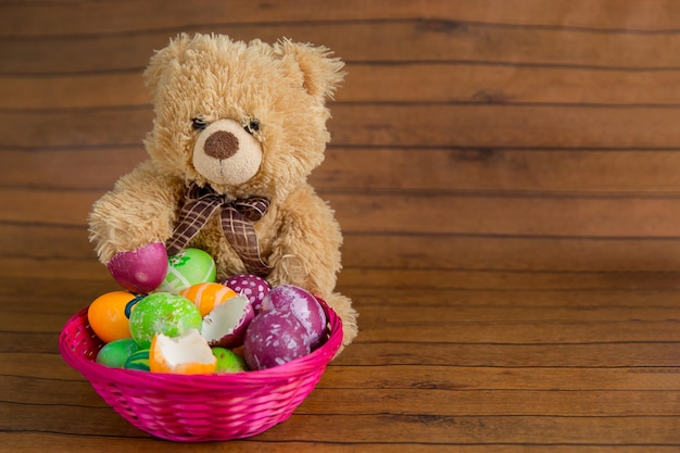 Huevos pintados de color Pascua en canasta y oso de peluche sobre fondo de madera decoración navideña de religión de abril