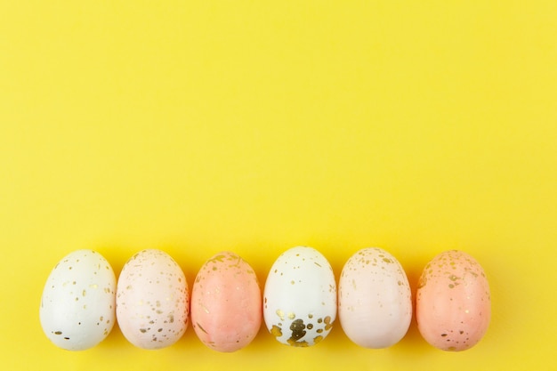 Huevos pintados de forma creativa en colores pastel decorados con pan de oro están dispuestos en fila sobre fondo amarillo