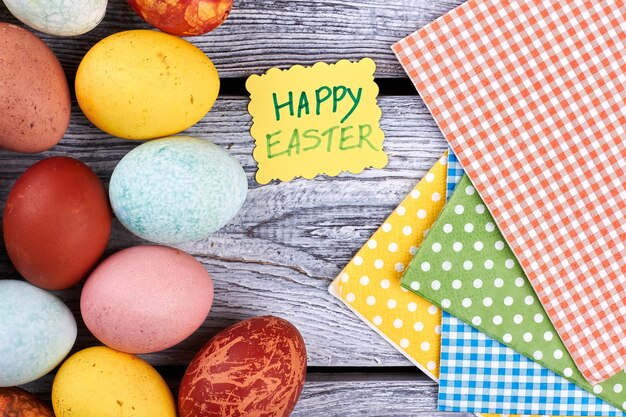 Huevos pintados y servilletas de colores Tarjeta de felicitación sobre fondo de madera Comida para Pascua