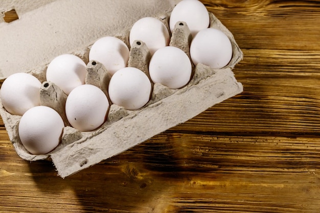 Foto huevos de pollo crudos en caja de huevos de cartón sobre mesa de madera vista superior