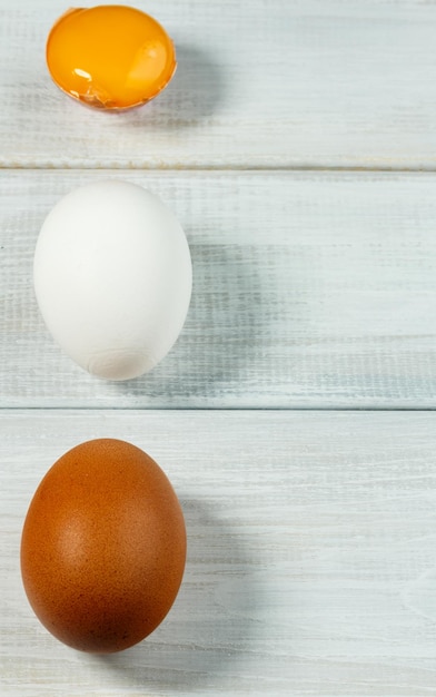 Huevos de pollo frescos Dos huevos de pollo enteros y uno agrietado sobre un fondo blanco de madera