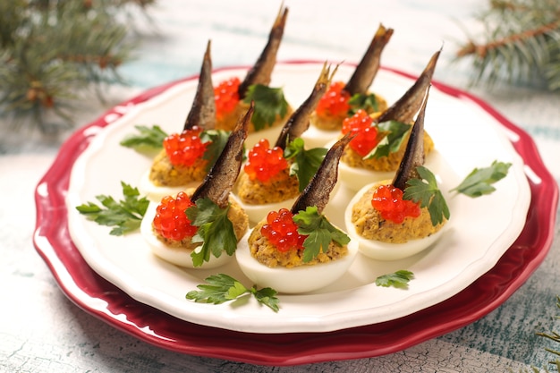 Huevos rellenos de espadines y caviar rojo en un plato blanco. Merienda festiva