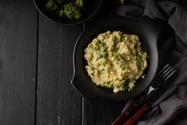 Huevos revueltos con brócoli y cebolla verde servido en plato oscuro con pan sobre mesa negra