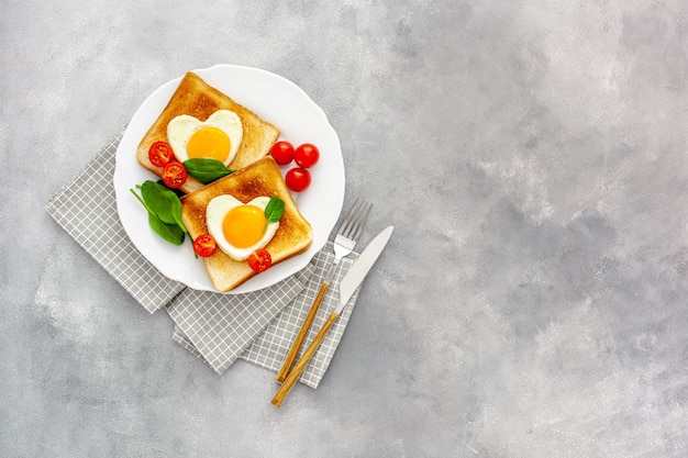 Huevos revueltos en forma de corazón en un plato con tomates, verduras y café