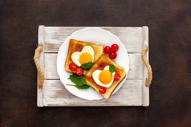 Huevos revueltos en forma de corazón en un plato con tomates, verduras y café