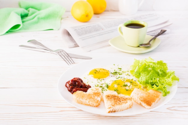 Huevos revueltos, pan frito, salsa de tomate y hojas de lechuga en un plato, taza de café y periódico sobre la mesa.