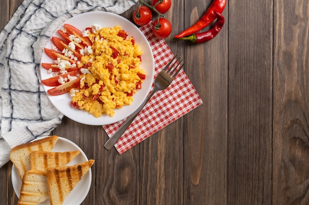 Huevos revueltos con pimiento, tomate y queso en mesa de madera