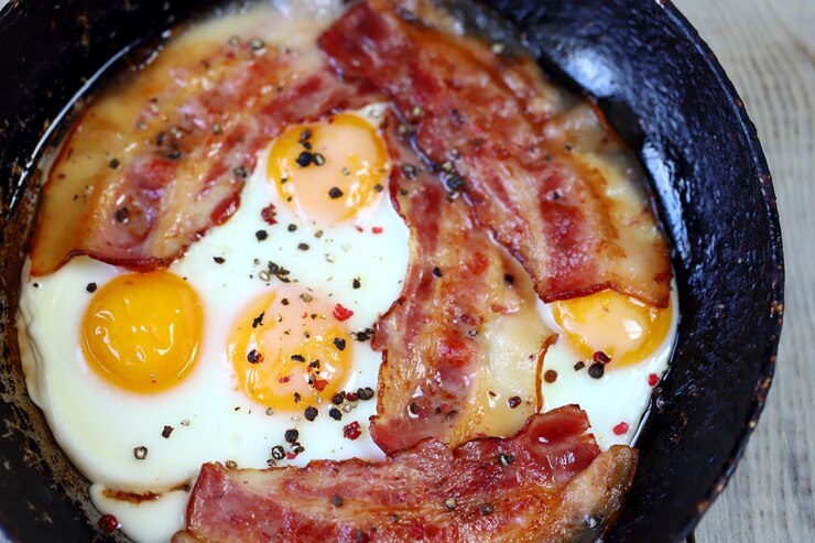 Foto huevos revueltos con tocino en una sartén sobre la mesa.