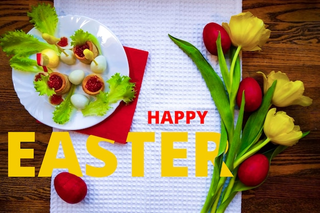 Foto los huevos rojos están sobre la mesa entre los tulipanes amarillos atados con una cinta escarlata un plato con huevos de codorniz nidos de caviar y una estatuilla de pollo hecha de yemas es el concepto de un plato de pascua