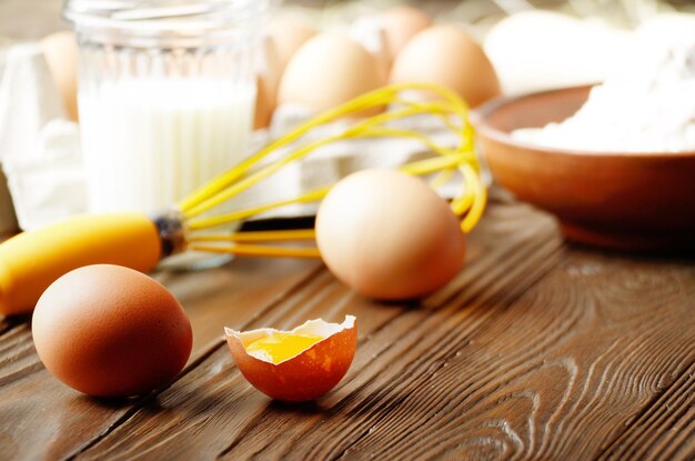 Huevos rotos de pollo marrón orgánico crudo con leche de harina de yema y batir en la mesa de madera de la cocina