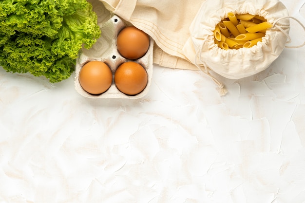 Huevos, salat y pasta en paquete ecológico sobre fondo de cemento blanco. Cero concepto de residuos. Compra de alimentos sin empaque. Vista superior Lugar para texto