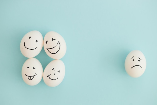 Huevos sonrientes y tristes sobre un fondo azul.