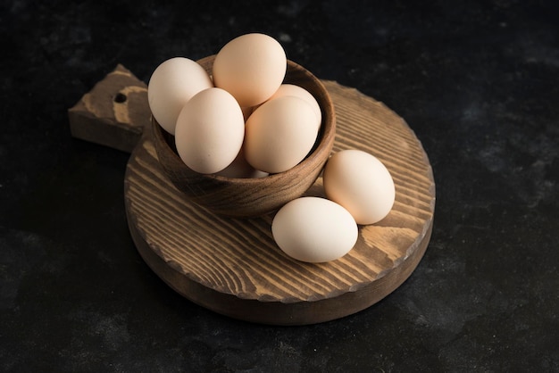 Huevos en tablero de madera en tazón de madera fondo oscuro